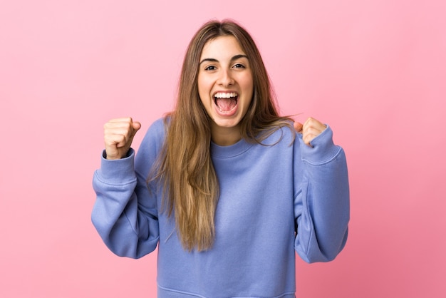 Junge Frau über isolierter rosa Wand, die einen Sieg in der Siegerposition feiert