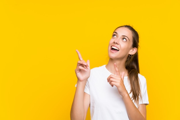 Junge Frau über lokalisiertem gelbem Hintergrund zeigend mit dem Zeigefinger eine großartige Idee