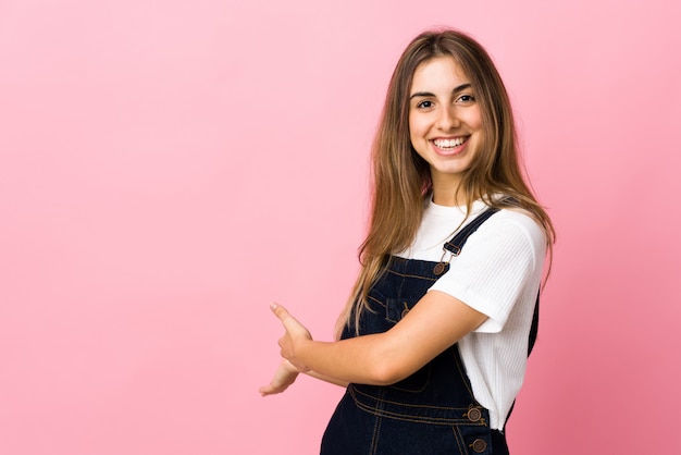 Junge Frau über rosa Wand, die Hände zur Seite für Einladung zum Kommen ausdehnt