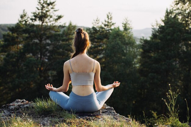 Junge Frau übt Yoga bei Sonnenuntergang oder Sonnenaufgang an einem wunderschönen Bergort