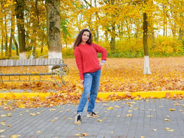 Junge Frau umgeben von gefallenem gelbem Laub im Park