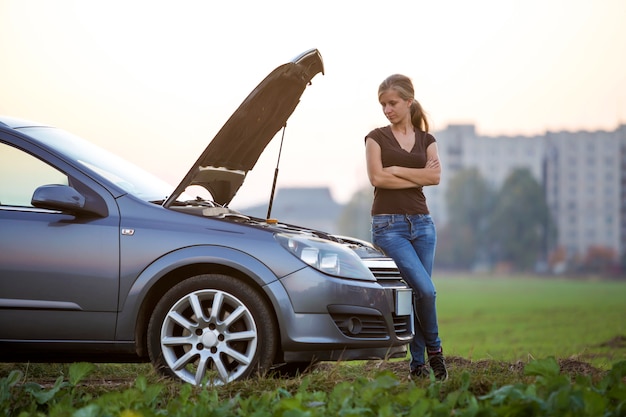 Junge Frau und ein Auto mit geknallter Motorhaube.