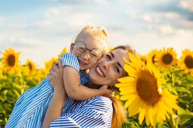 Junge Frau und ein kleines Mädchen in ihren Armen auf einem Sonnenblumenfeld. Mama mit dem Kind.