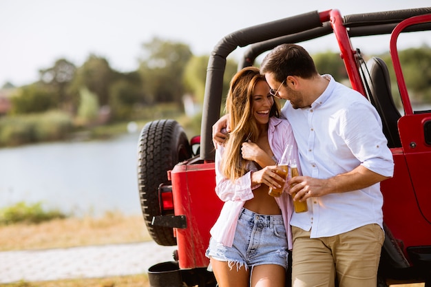 Junge Frau und Mann, die den Spaß im Freien nahe rotem Auto am Sommertag hat