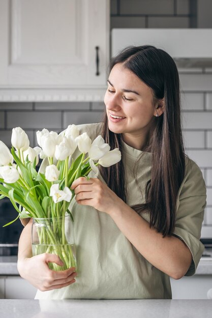 Junge Frau und Vase mit einem Bouquet weißer Tulpen in der Küche