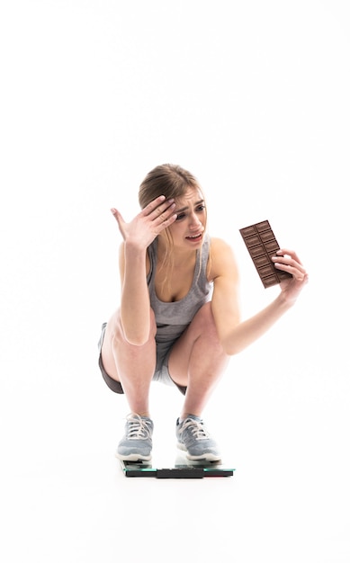 Junge Frau unglücklich mit ihrem Gewicht, das Schokolade hält, lokalisiert auf Weiß.
