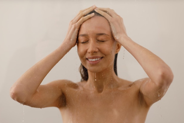 Junge Frau unter den Wassertropfen in der Dusche Schönes Mädchen unter dem Wasserstrahl auf isoliertem Hintergrund Wet happy face