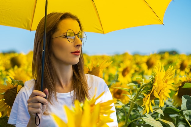 Junge Frau unter gelbem Regenschirm am Sonnenblumenfeld.