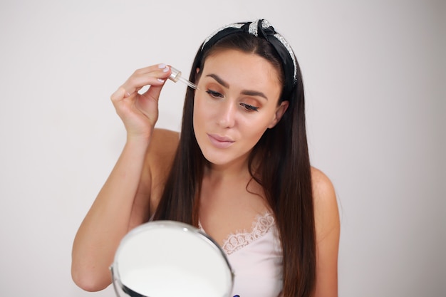 Junge Frau vor einem Spiegel, der Gesichtspflegeprodukte anwendet