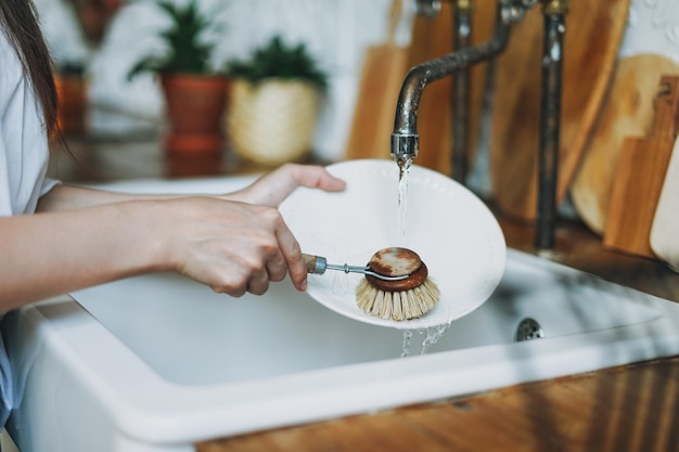 Foto junge frau wäscht das geschirr mit einer holzbürste mit natürlichen borsten am fenster in der küche