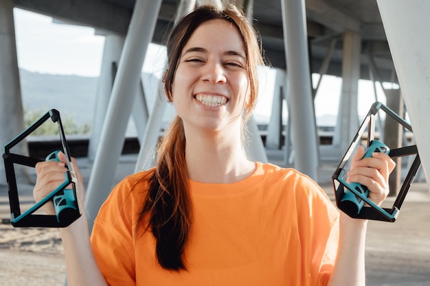 Junge Frau zeigt Push-up-Grabber-Tools für die Kamera, während sie glücklich lächelt mit neuem Kauf Sport und gesunder Lebensstil in Inhalten sozialer Netzwerke Städtisches und sonniges Szenario