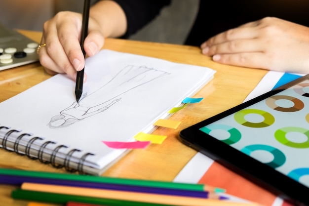 Junge Frauen arbeiten als Modedesigner Zeichnung Skizzen für Kleidung in Atelier Papier am Arbeitsplatz Studio.