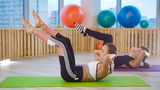 Junge Frauen beim Fitnesstraining im Studio Beinübungen auf einer Yogamatte