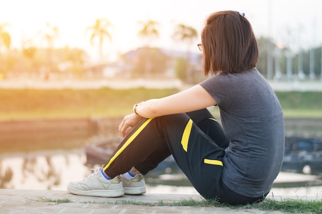 Junge Frauen, die auf dem Boden nahe dem See für Rest sitzen, nachdem eine Übung getan worden ist