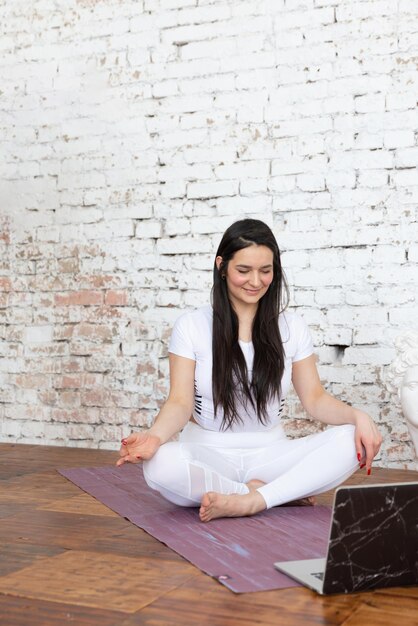 Junge Frauen, die von zu Hause aus nach einem Online-Training am Computer oder online trainieren oder Yoga machen