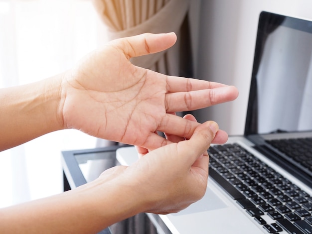 Junge Frauen haben Fingerspitzen, schmerzende Finger, Hand- und Handschmerzen durch die Arbeit mit einem Laptop, Entzündungen der Nerven und Gelenke.