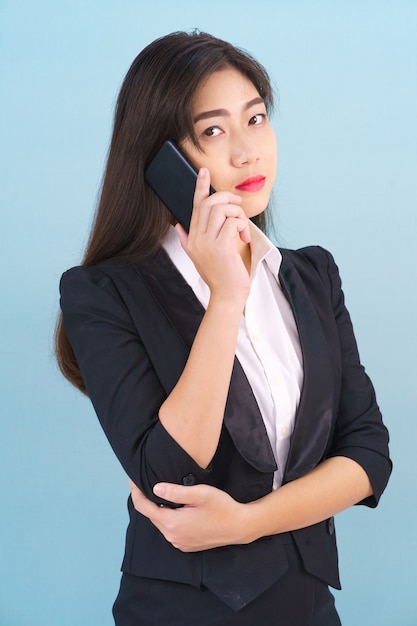 Junge Frauen im Anzug, die ihr Telefon vor blauem Hintergrund halten