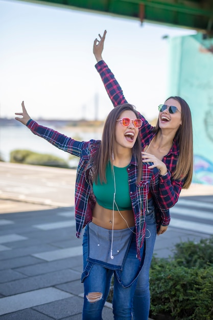 Foto junge frauen im freien auf der straße hören musik über kopfhörer und haben spaß