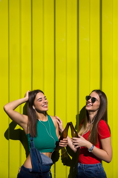 Foto junge frauen im freien gegen grüne wand hören musik über kopfhörer und haben spaß