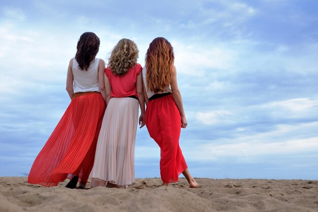 Junge Frauen in einem langen Kleid stehen am Sommerabend am Strand