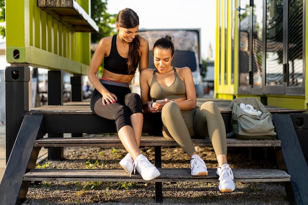 Junge Frauen in Sportbekleidung, die nach dem Training auf das Handy schauen