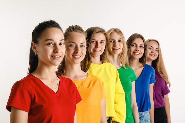 Junge Frauen trugen in LGBT-Flaggenfarben lokalisiert auf weißer Wand. Kaukasische weibliche Modelle in hellen Hemden. Sieh glücklich aus und lächle. Vertrauen Sie auf LGBT-Stolz, Menschenrechte und das Konzept der Wahlfreiheit.