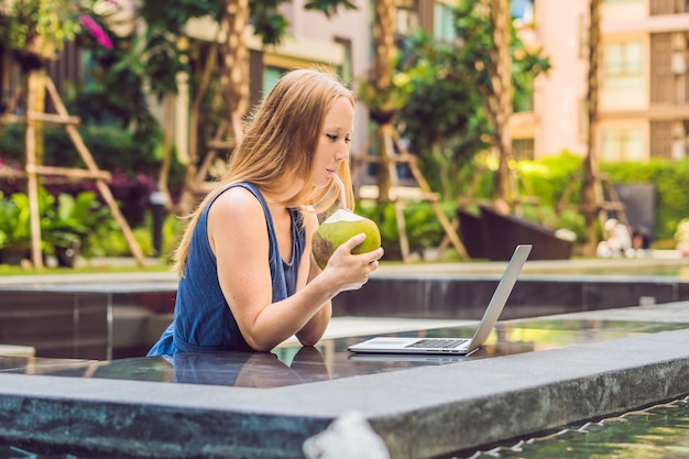 Junge Freiberuflerin sitzt am Pool mit ihrem Laptop im Hotel und surft in ihr