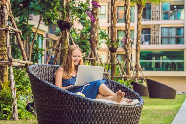 Junge Freiberuflerin sitzt am Pool mit ihrem Laptop im Hotel und surft in ihrem Smartphone. In den Ferien beschäftigt. Fernarbeitskonzept. Kopieren Sie Platz für Ihren Text.