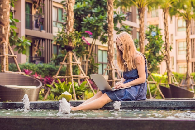 Junge Freiberuflerin sitzt am Pool mit ihrem Laptop im Hotel und surft in ihrem Smartphone. In den Ferien beschäftigt. Fernarbeitskonzept. Kopieren Sie Platz für Ihren Text.
