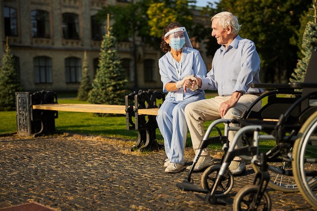 Junge Freiwillige, die Hände eines lächelnden älteren Mannes im Freien halten