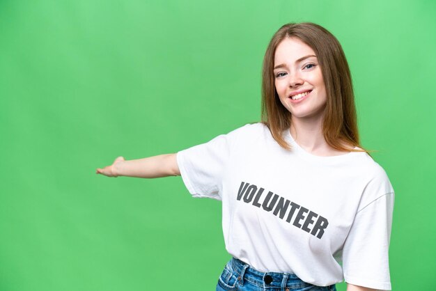 Junge freiwillige Frau über isoliertem Chroma-Key-Hintergrund, die die Hände zur Seite streckt, um zum Kommen einzuladen