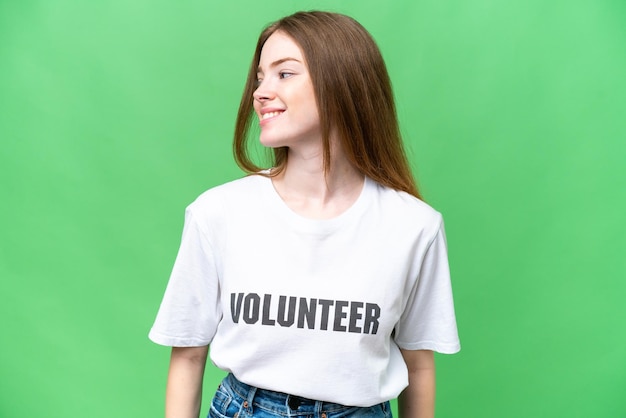 Junge freiwillige Frau über isoliertem Chroma-Key-Hintergrund mit Blick auf die Seite