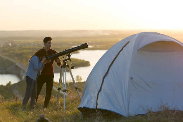 Junge Freunde, die am Sommerabend horizontal durch das Teleskop auf dem Hügel schauen