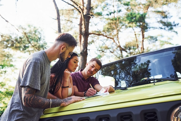 Junge Freunde, die Karte lesen, die auf der Haube des modernen grünen Jeeps im Wald ist.