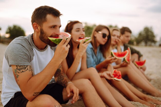 Junge Freunde entspannen sich am Strand und essen Wassermelone. Menschen im Sommer