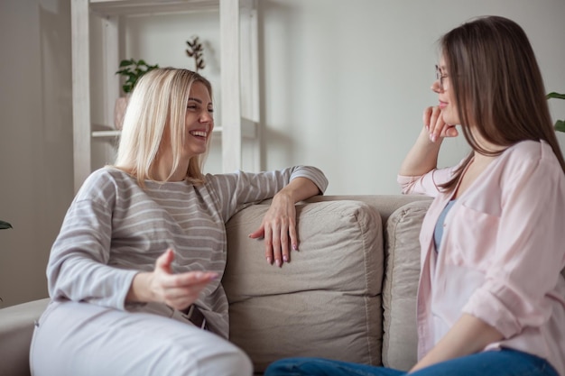 Junge Freundinnen sprechen lächelnd zusammen und sitzen zu Hause auf dem Sofa