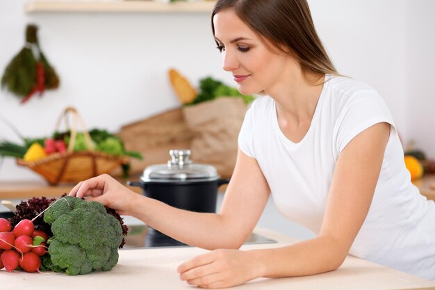 Junge fröhliche lächelnde Frau ist bereit zum Kochen in einer Küche Hausfrau, die am Tisch sitzt und in die Kamera schaut