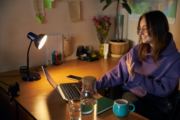 Junge fröhliche, selbstbewusste und glückliche Freiberuflerin arbeitet abends zu Hause am Laptop laptop