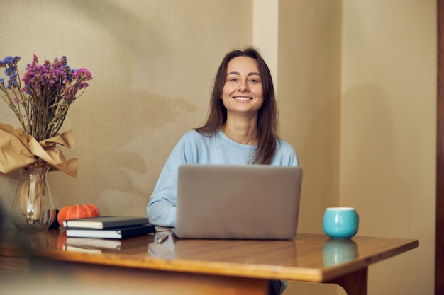 Junge fröhliche, selbstbewusste und glückliche Freiberuflerin arbeitet zu Hause in ihrer Küche am Laptop