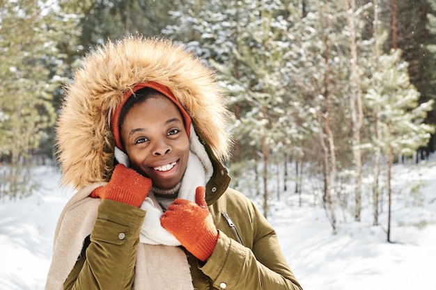 Junge, fröhliche, zeitgenössische schwarze Frau in Handschuhen, Winterjacke und Schal