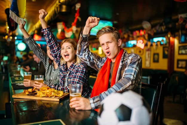 Junge Fußballfans feiern den Sieg ihrer Lieblingsmannschaft an der Theke in der Sportbar.