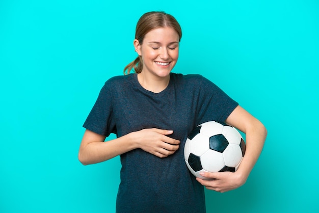 Junge Fußballspielerin isoliert auf blauem Hintergrund, die viel lächelt
