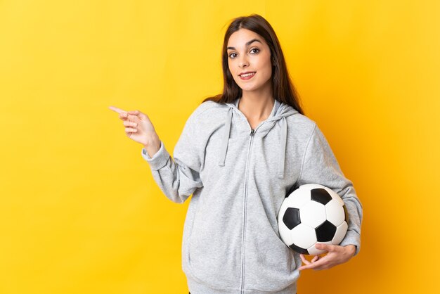 Junge Fußballspielerin lokalisiert auf gelber Wand, die Finger zur Seite zeigt