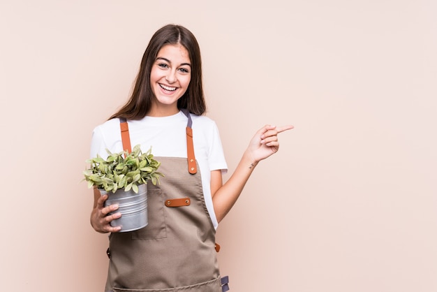 Junge Gärtnerfrau, die ein plantmiling hält und beiseite zeigt und etwas auf Leerstelle zeigt