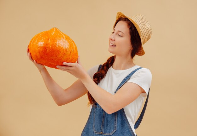 Junge Gärtnerin betrachtet einen reifen Bio-Kürbis auf einem gelben Hintergrundkonzept von Halloween