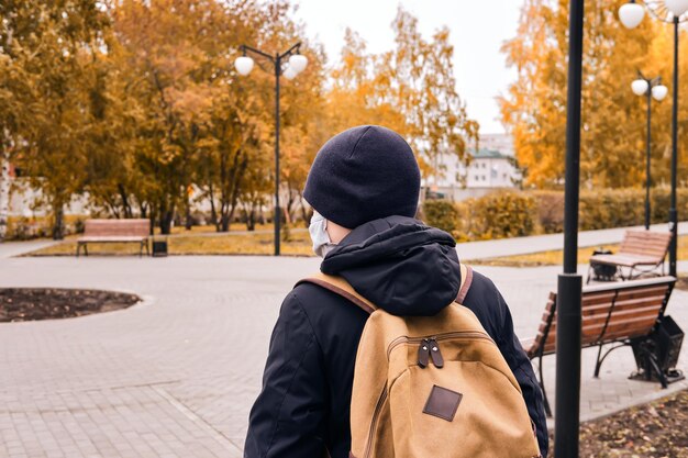 Junge geht während der Coronavirus-Pandemie mit Schutzmaske zur Schule. Neue Normalität. Rückansicht.