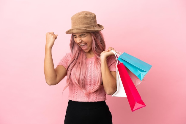 Junge gemischte Frau mit Einkaufstasche auf rosa Hintergrund isoliert einen Sieg feiernd