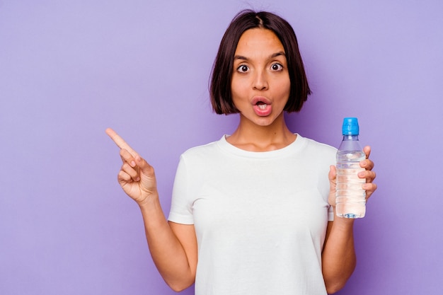 Junge gemischte Rasse, die eine Wasserflasche lokalisiert auf purpurrotem Hintergrund hält, der zur Seite zeigt