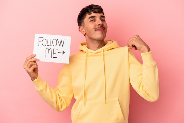Junge gemischte Rasse Mann hält ein Follow-me-Plakat isoliert auf rosa Hintergrund