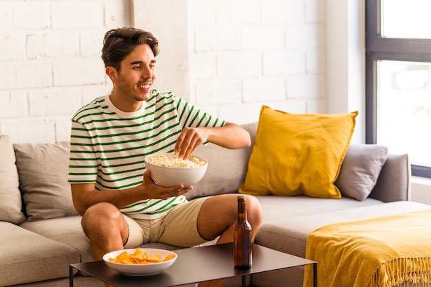 Junge gemischte Rasse Mann isst Popcorn auf dem Sofa sitzend